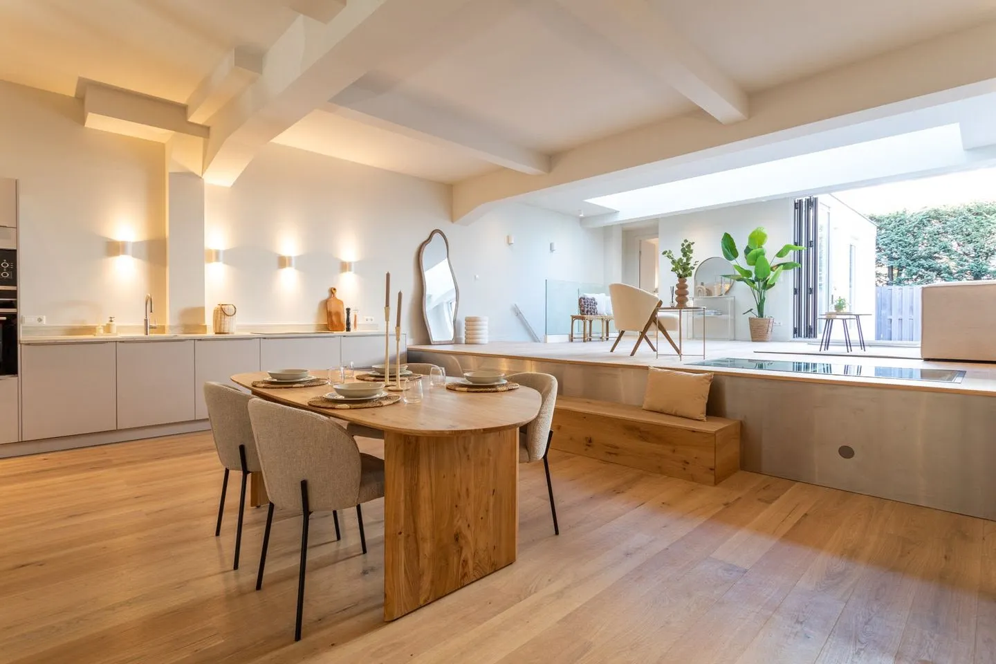 Open woonkeuken met een ovale houten eettafel, bouclé stoelen, wandlampjes en een lichtstraat
