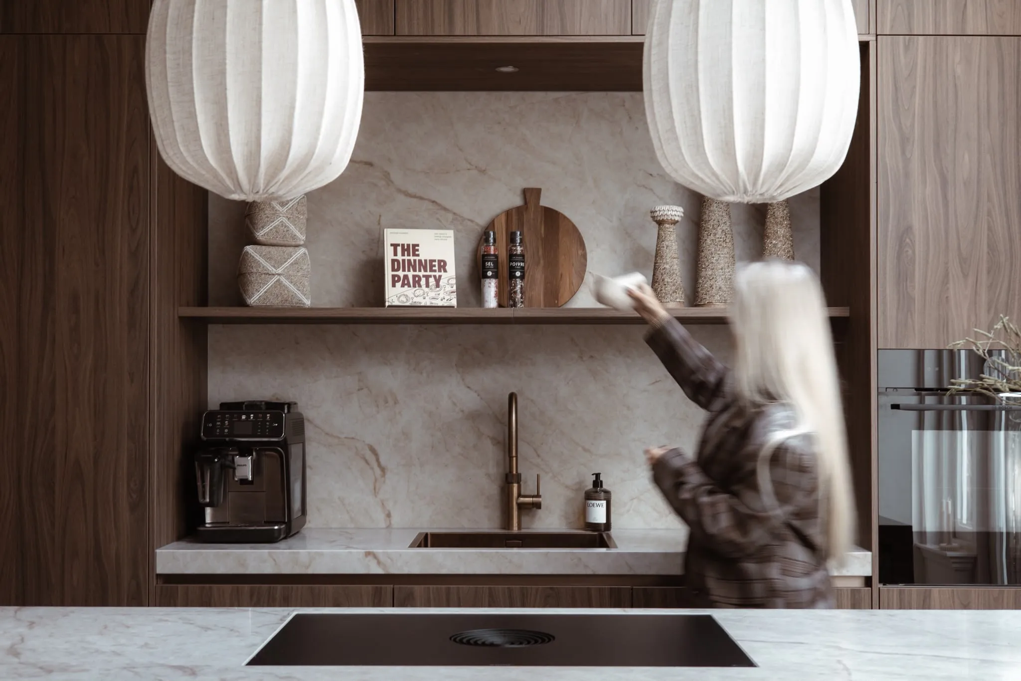 Melissa zet een kom op het schap in een notenhouten keuken met een marmeren achterwand en linnen hanglampen