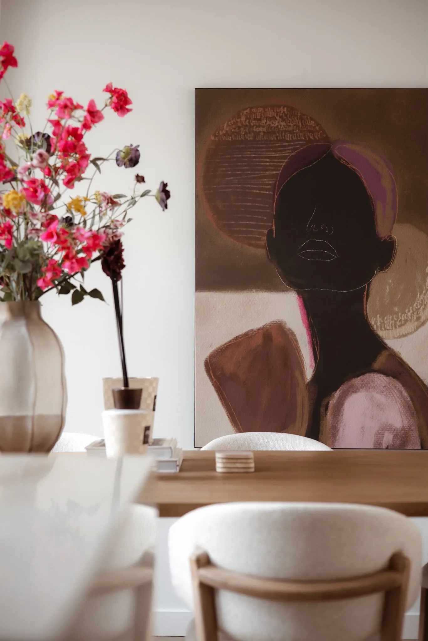 Eettafel met bouclé stoelen, een vaas met roze bloemen en een groot portretschilderij in bruine en roze tinten